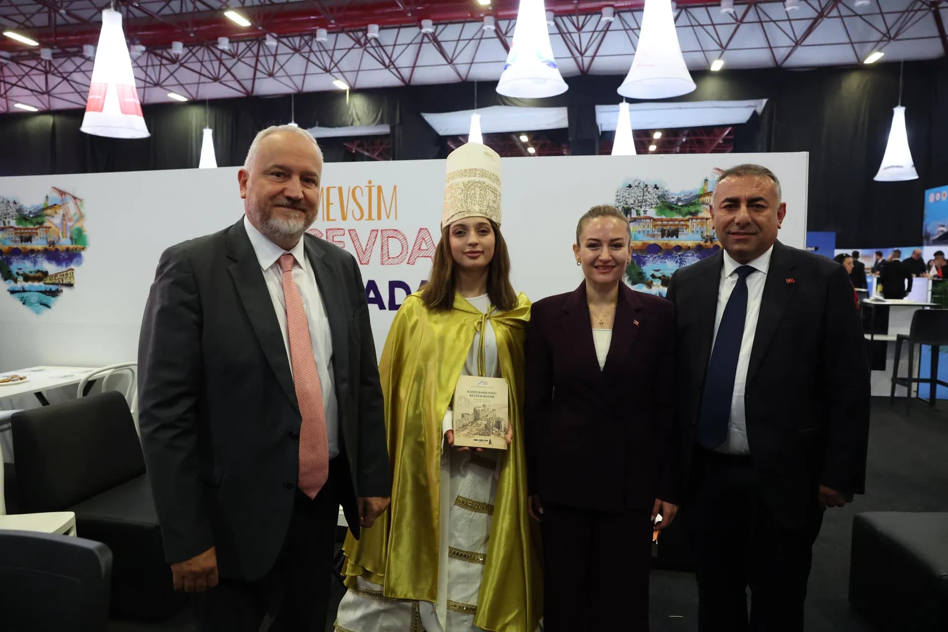 Büşra Özdemir yanında yöresel kıyafetli bir kadın ve iki erkekle turizm fuarında 