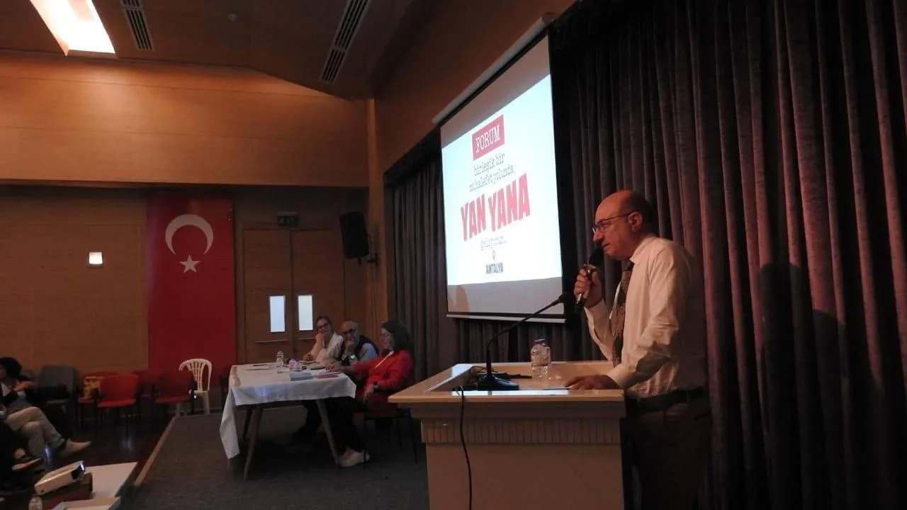 Kürsüde konuşan bir erkek sağ tarafında ekran var 