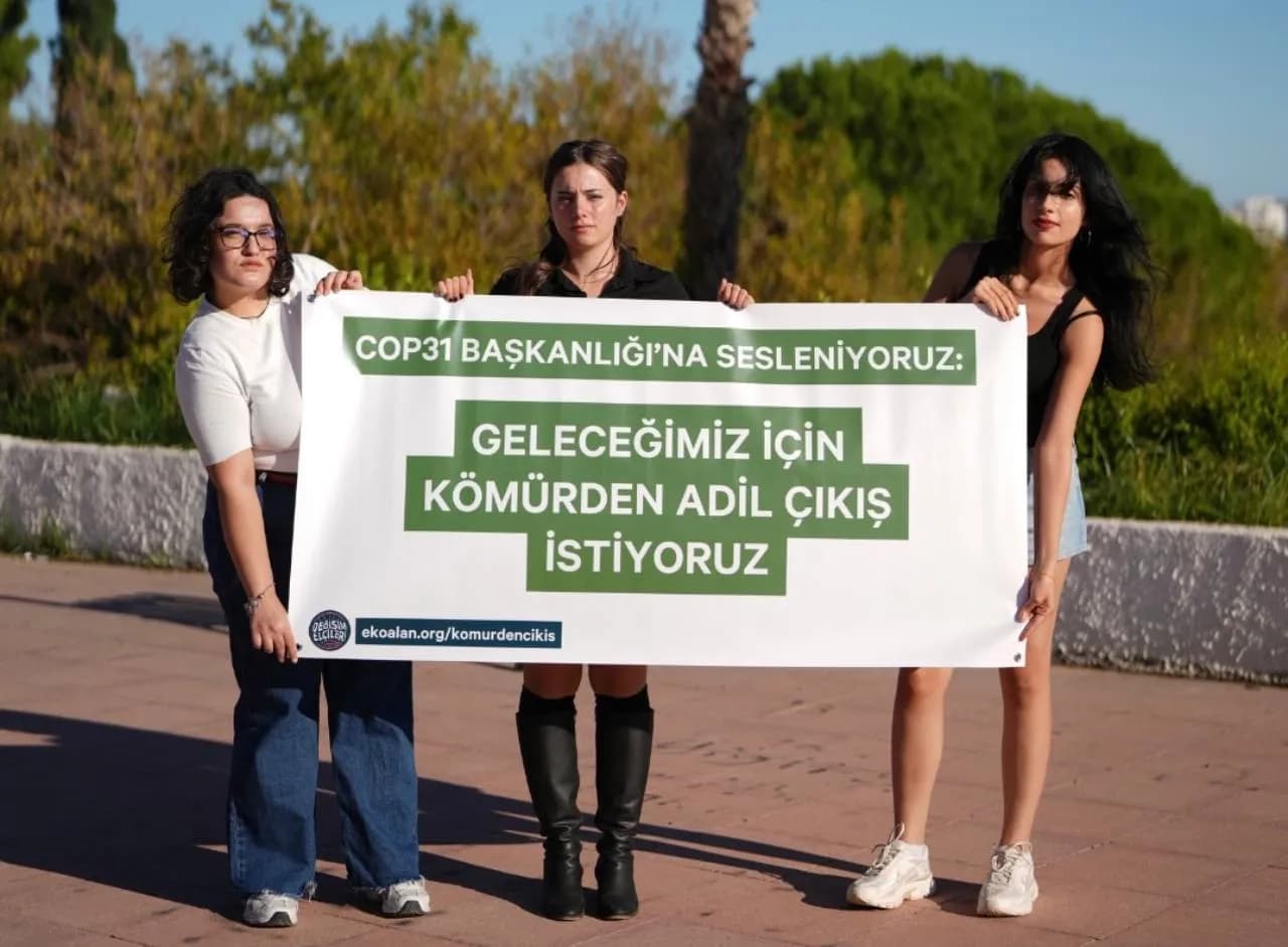 Üç genç kadın öğrenci ellerinde kömürden adil çıkış istiyoruz pankartıyla yer alıyor