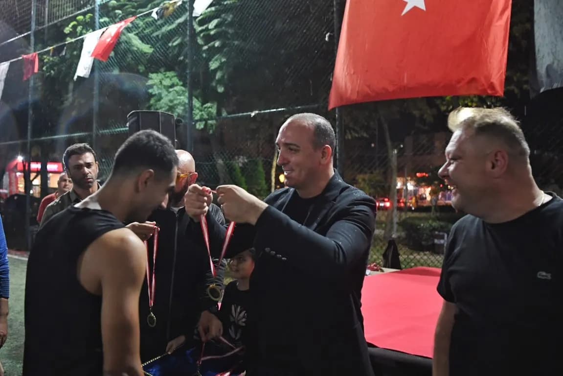 Cem Kotan futbolda şampiyon olan bir erkeğe madalya takıyor